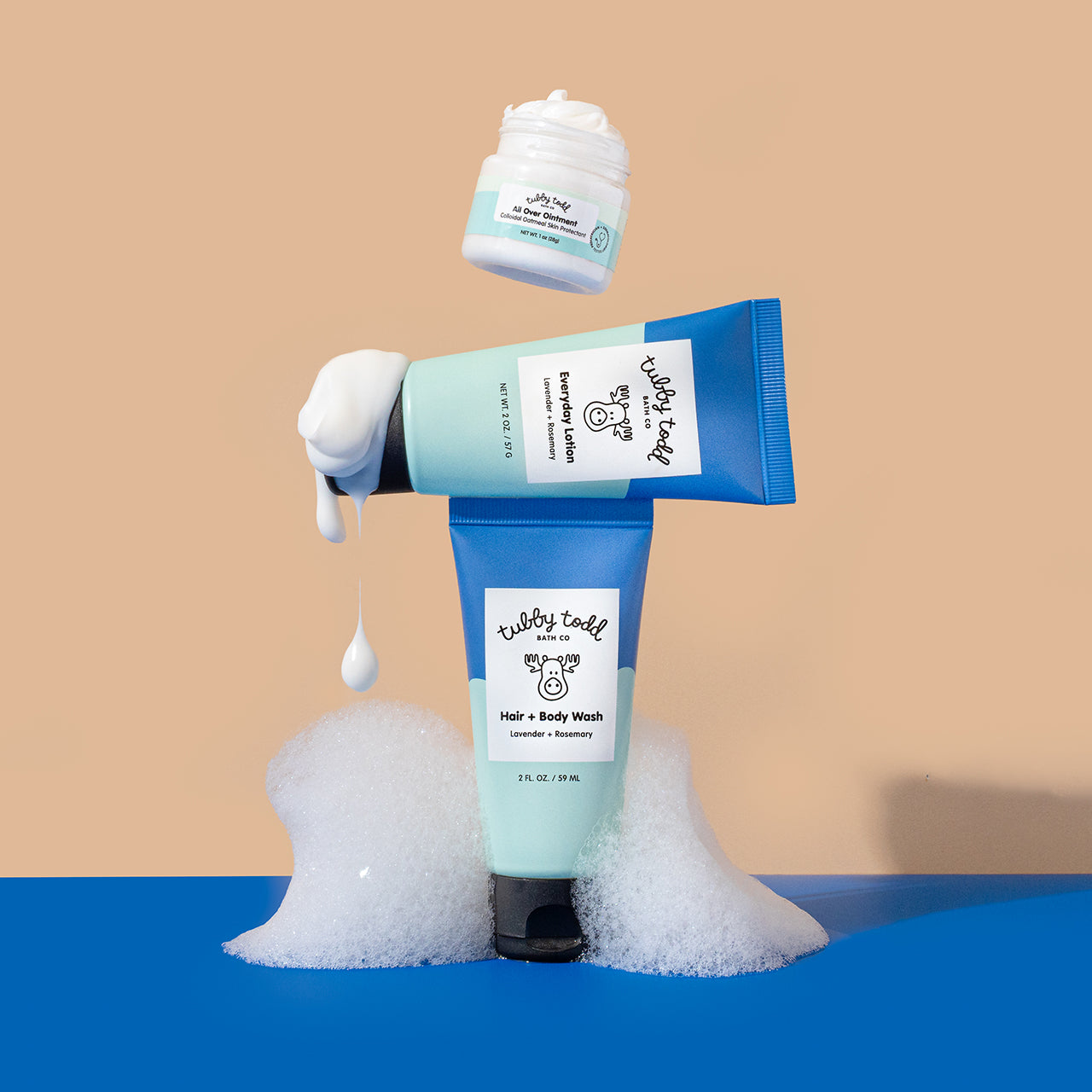 The Lavender Rosemary 2oz Hair + Body + Wash, Everyday Lotion tubes are standing with showing the texture on the color block background and 1oz All Over Ointment OTC jar floating opened.